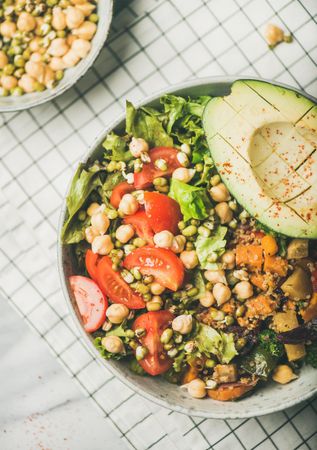Healthy vegan lunch bowl with avocado, grains, vegetables, on checkered napkin