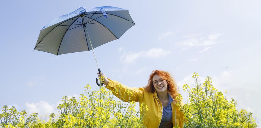 Joyful woman holding umbrella in yellow field on sunny day