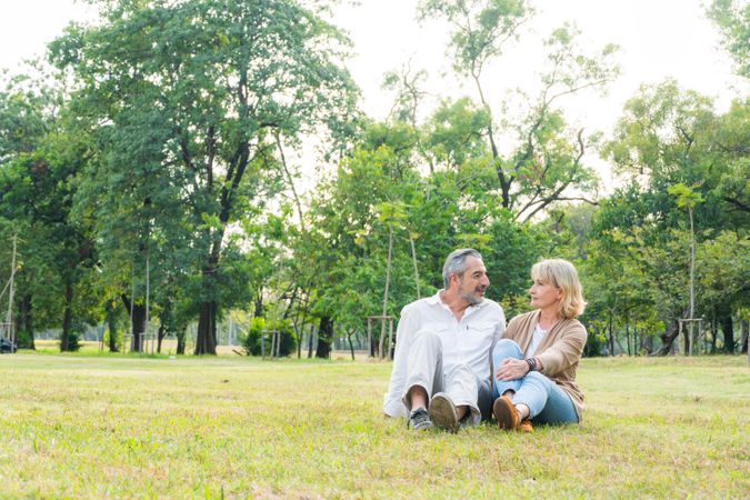 Mature couple sitting in green grass surrounded by trees