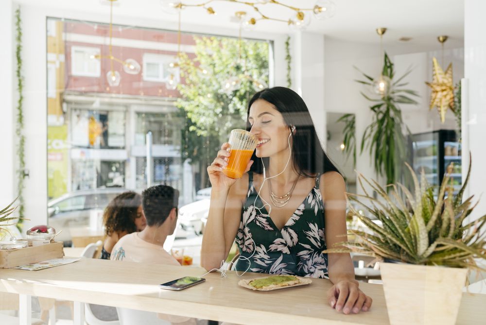 Woman with healthy drink listening to music in cafe
