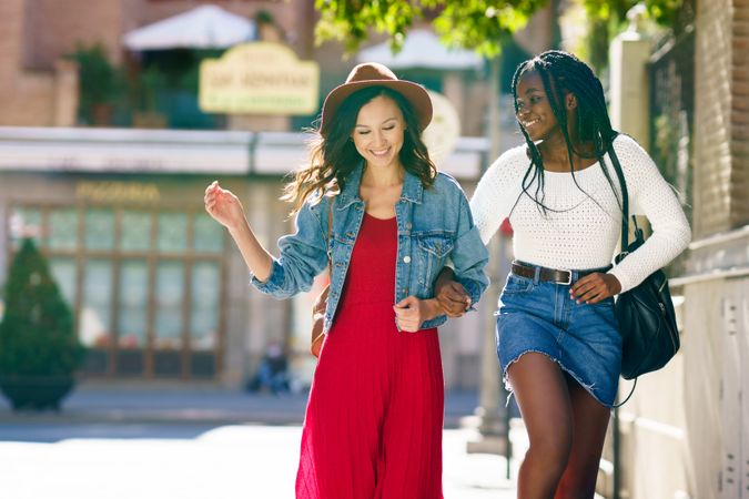 Female friends strolling down a sunny street arm in arm