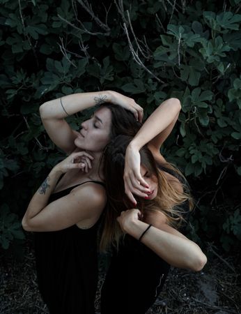 Young women posing near green bush