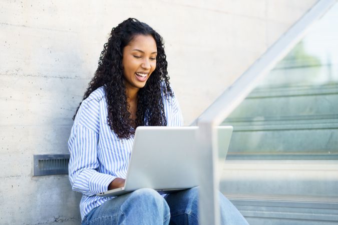A Young Woman is Engaged in Working on Her Laptop Outdoors Within a Modern Urban Setting