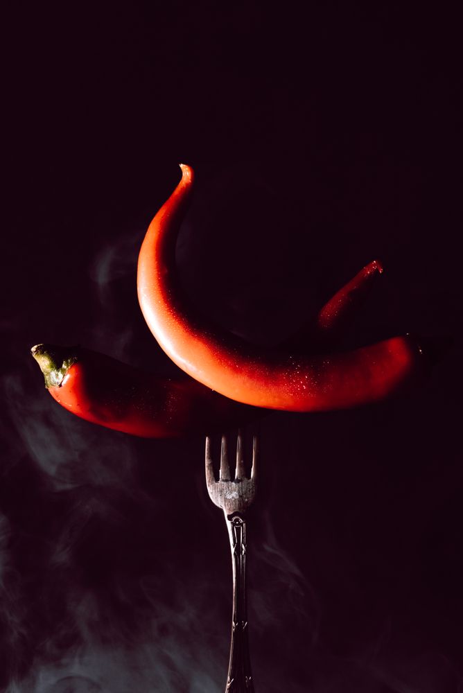 two red chili pepper in fork on a dark background with smoke