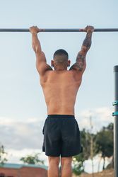 back view of a male athlete doing pull ups on a bar outdoors, calisthenics