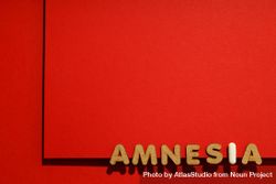 Cork letters of the word “Amnesia” with pill along bottom of red background with copy space bE1lnb