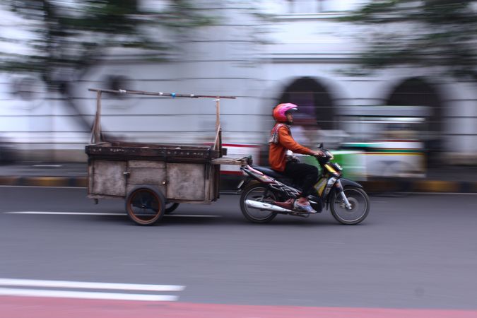 Long shot photo of man riding bicycle with trolley on road