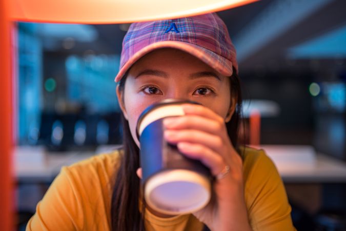 Asian woman drinking coffee at table under lighting lamp