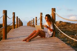 Woman using laptop and mobile phone sitting on bridge