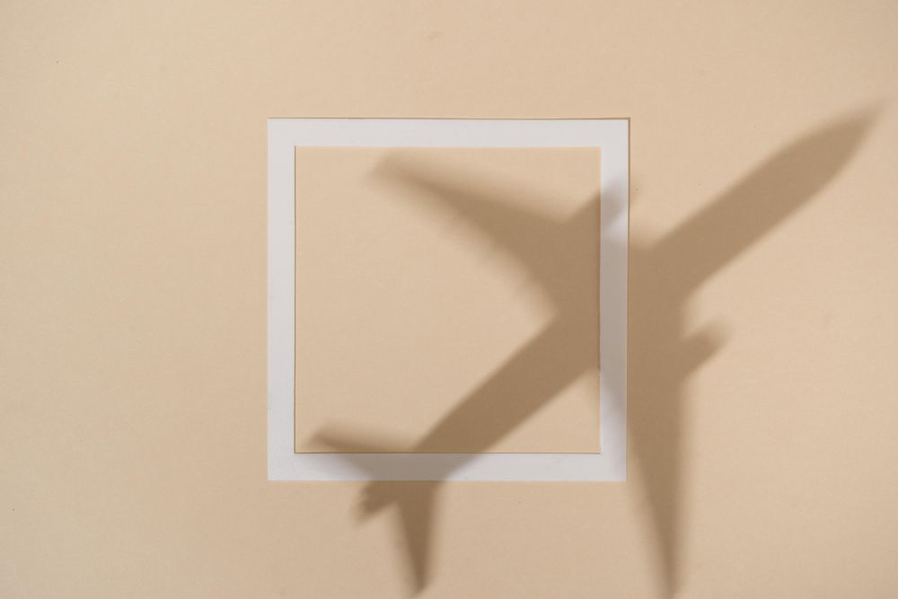 Shadow of airplane over beige paper background with square