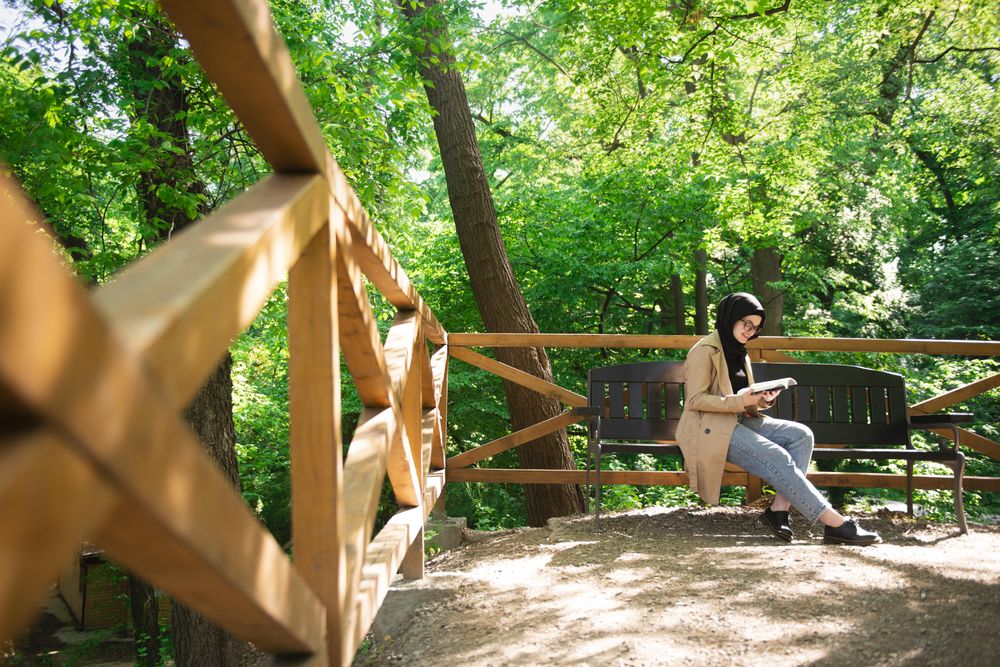 Middle Eastern woman reading on park bench under trees