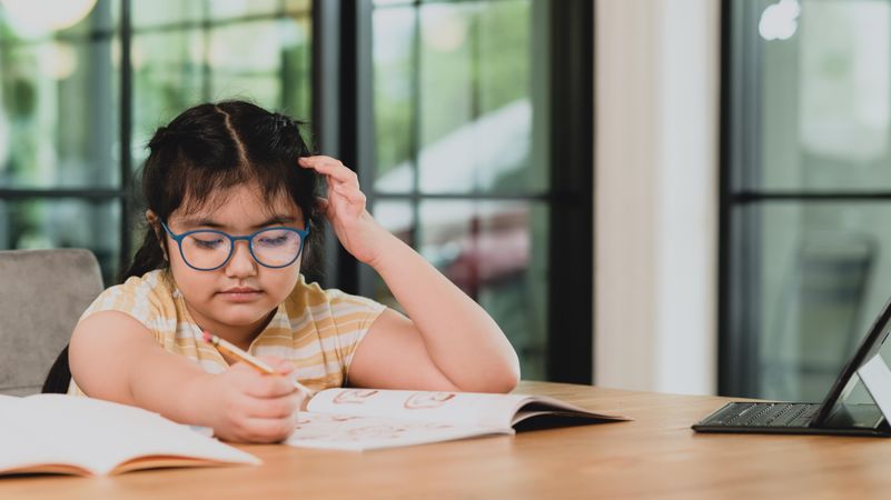 Asian girl doing homework out of her workbook