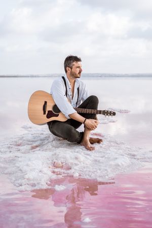 Musician with guitar on pink sandy water