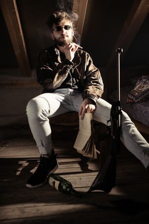 Man in eyeglasses smoking cigarette near bottle and gun