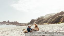 Mature couple relaxing on beach sand with their pet dogs 4BGQkb