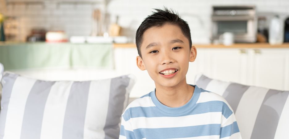 Portrait of Asian boy sitting on couch in the living room looking at camera