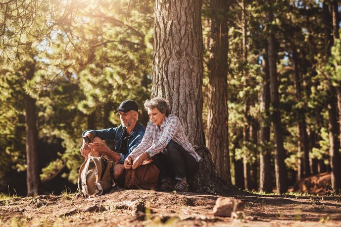 Portrait of mature couple sitting together under a tree with backpacks and compass