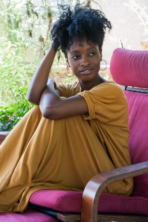 Woman model with curly hair and hoop earrings sitting outside smiling and looking away