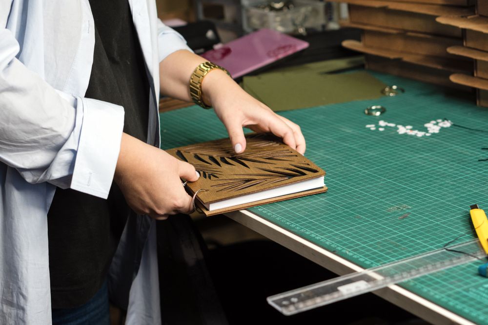 Female hands hold notebook with removable blocks and wooden cover together in workshop