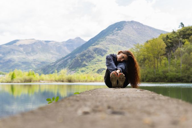 Traveling woman sitting on pier near lake in highlands