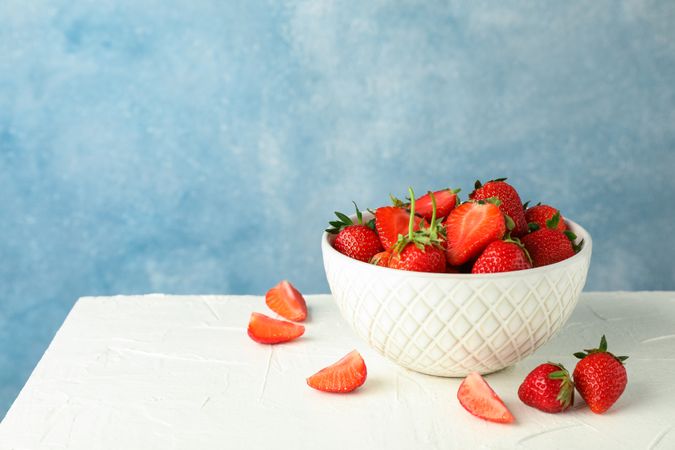 Bowl with fresh strawberries on table against blue background, space for text. Summer sweet fruits and berries