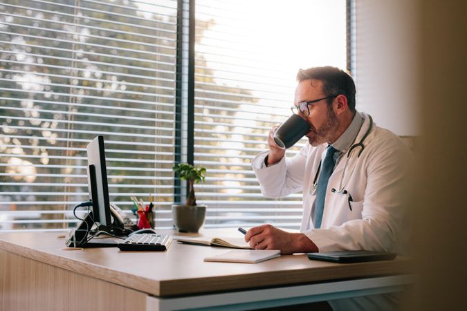 Male doctor drinking coffee at his desk