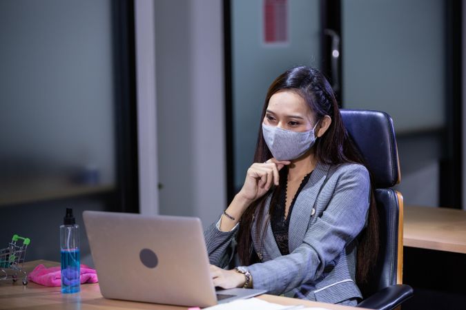 Asian woman in protective mask using laptop working overtime at desk in the office