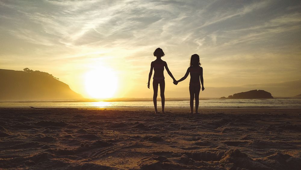 Silhouettes of two girls holding her hands in the beach at sunset