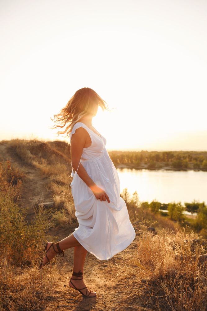 Blonde female in ethereal summer dress looking back at lake