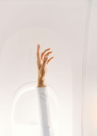 Person in white sweater raising hand up in plane