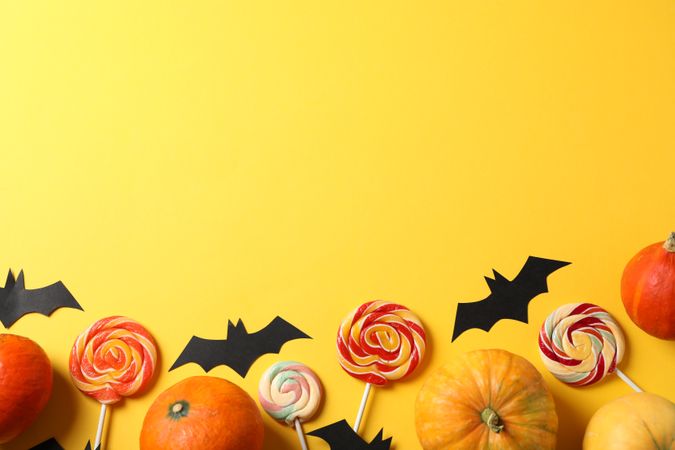 Candy, decorative bats and pumpkins on yellow background, top view