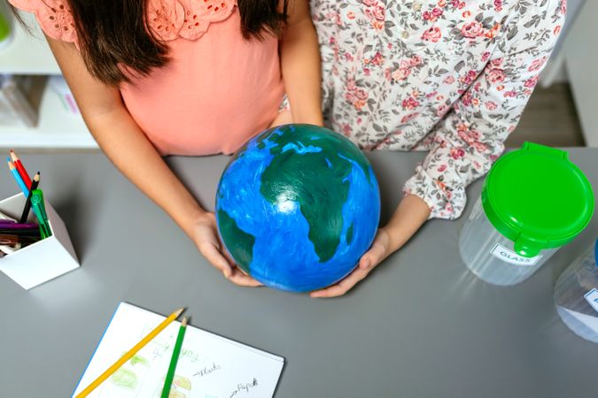 Two unrecognizable female students holding handmade globe world earth