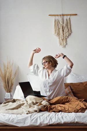 Woman Working From Home Stretching In Bed With Phone