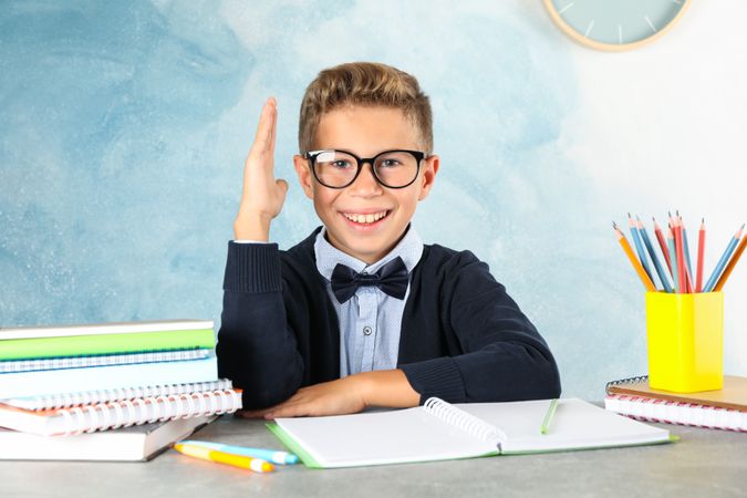 Boy in school uniform sitting at the table against color background