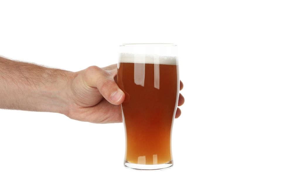 Hand holds glass of beer, isolated on light background