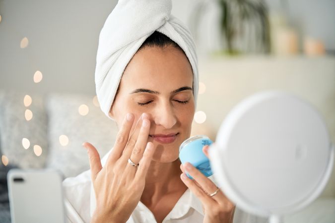 Relaxed woman applying cream on face while taking video