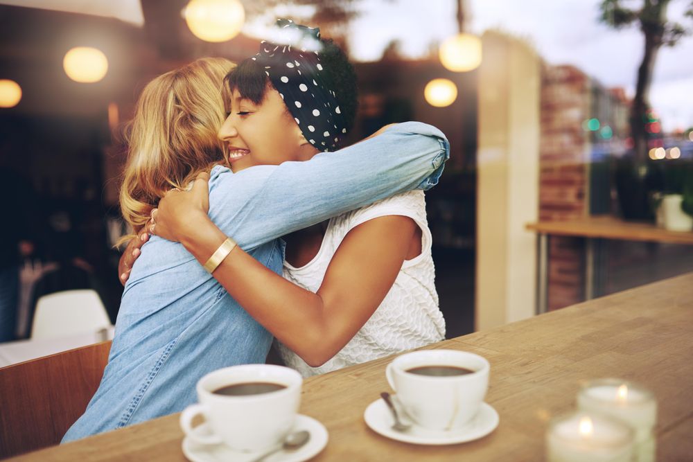 Two female friends hugging in a cafe window
