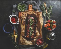 Roasted BBQ ribs with homemade pesto, pickled vegetables, sauces and rosemary on dark concrete kitchen table