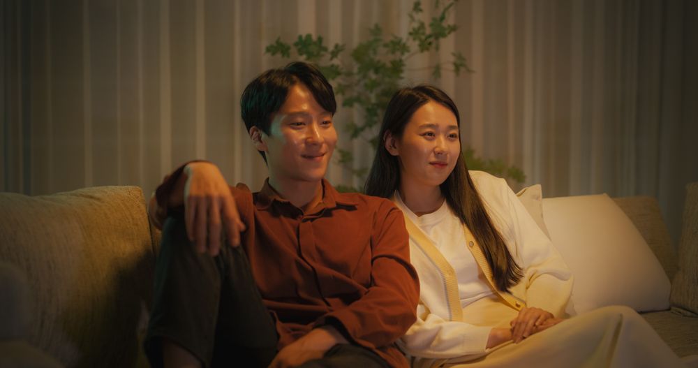 Portrait of a Young South Korean Couple Spending Time at Home, Sitting Together on a Sofa.