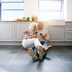 Square shot of smiling mature couple drinking red wine together on kitchen floor