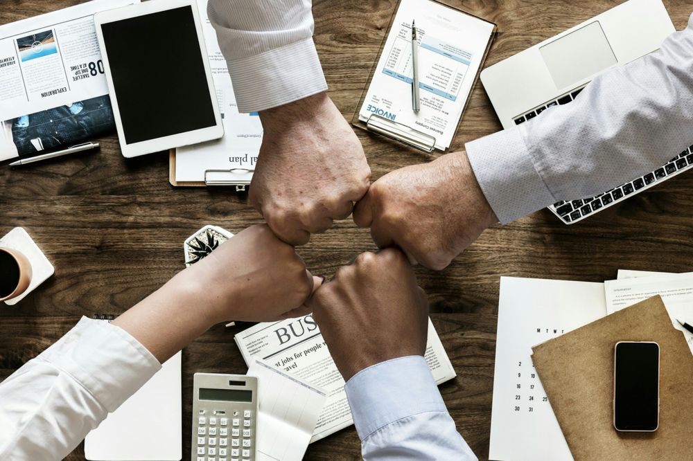 Collaborative Teamwork Fist Bump Among Office Workers at Workplace Desk