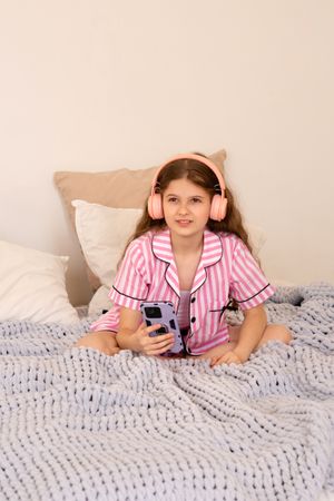 Young girl with headphones using smartphone on bed.
