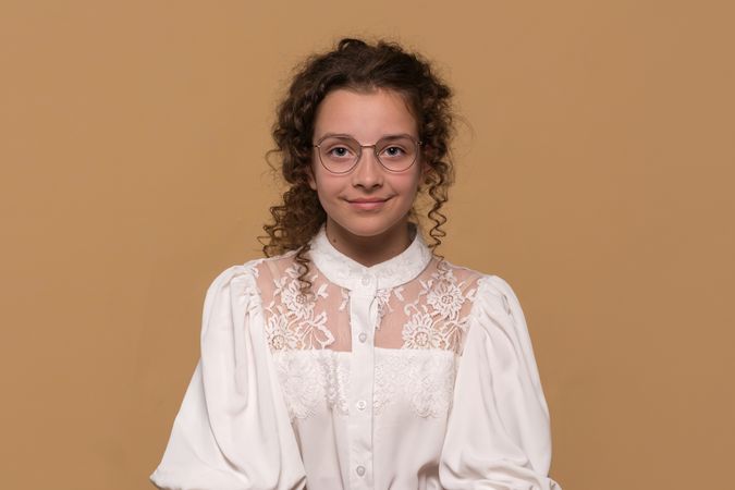 Girl with curly hair and glasses smiling, wearing lace blouse.