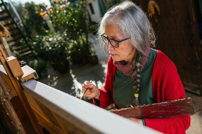 Older woman painting on canvas in garden