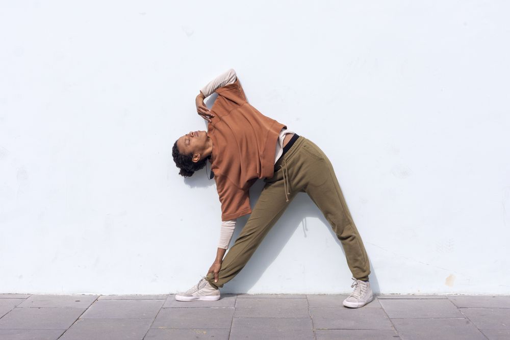 Stylish young female runner in sportswear doing warm-up routine outdoors before running against wall