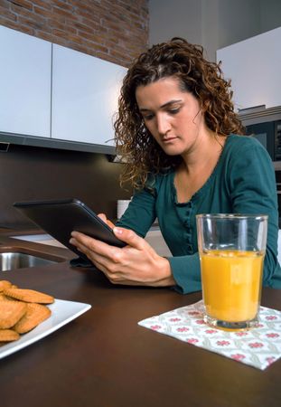 Female reading digital tablet next to cup of orange juice