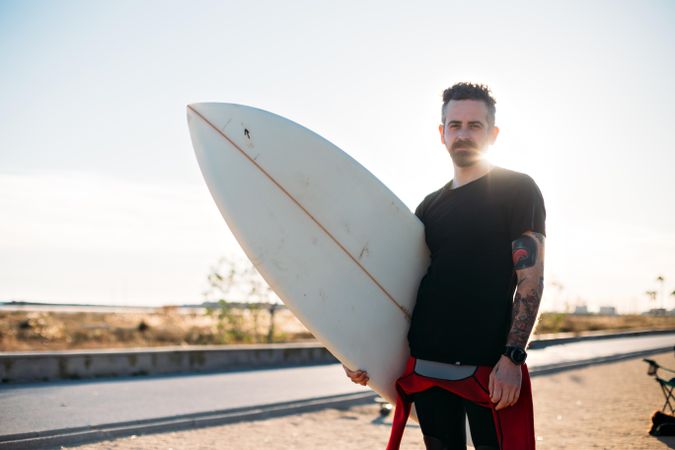 Man standing on road holding surfboard