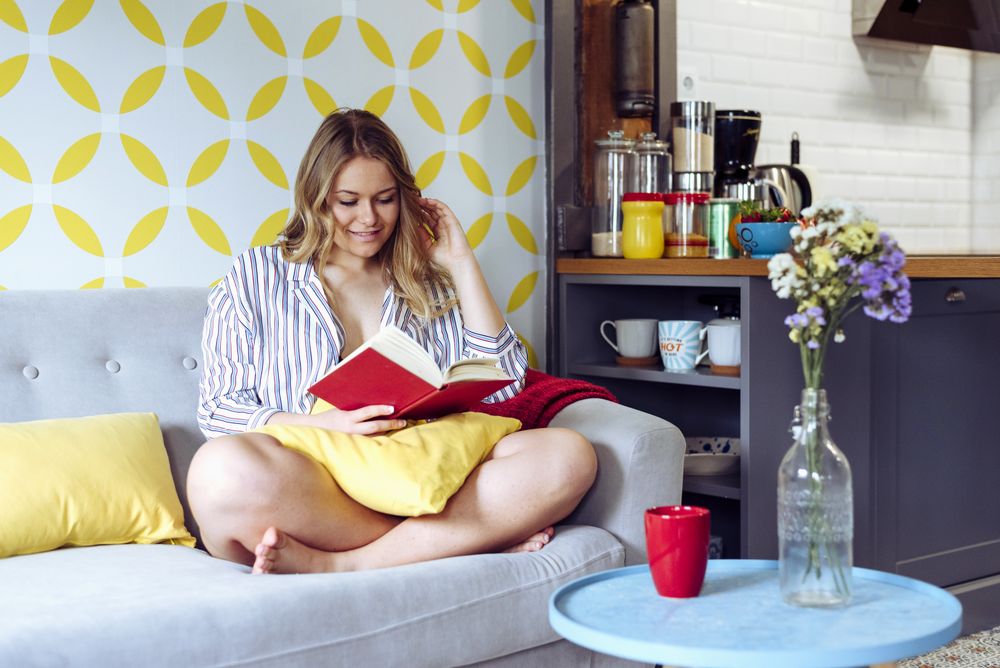 Young happy female reading book on sofa