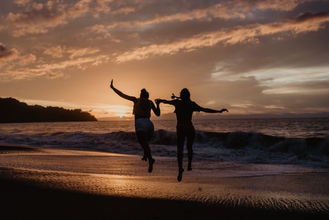 Unrecognizable women jumping towards waving sea