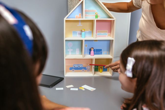 Unrecognizable teacher explaining to her students the parts of a sustainable house pointing an electric car
